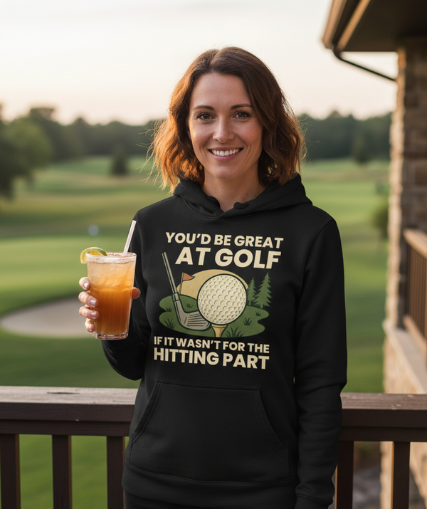 Woman wearing a hoodie with a humorous golf-themed message, holding a drink on a golf course. The lady is wearing a Cows Corner hoodie with the golf slogan 'You’d Be Great at Golf if It Wasn’t for the Hitting Part'. Cows Corner gifts are perfect for sport-mad fans, these gifts work brilliantly for birthdays, new baby celebrations, Father’s Day, Mother’s Day, Christmas, anniversaries, thank you gifts, end-of-season team awards, graduations, retirements, and just-because moments when you want to raise a smile
