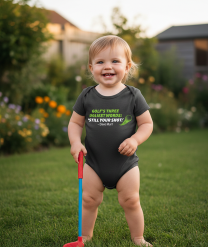 Child wearing a black onesie with text in a garden.  The baby is wearing a Cows Corner baby grow with a funny golf slogan 'Golf’s There Ugliest Words: ’Still Your Shot! – Dave Marr'. Cows Corner gifts are perfect for sport-mad fans, these gifts work brilliantly for birthdays, new baby celebrations, Father’s Day, Mother’s Day, Christmas, anniversaries, thank you gifts, end-of-season team awards, graduations, retirements, and just-because moments when you want to raise a smile. 
