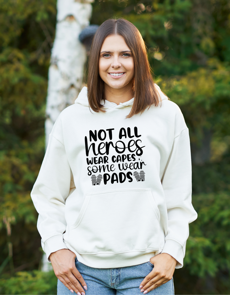 A lady wearing a white hoodie with Not All Heroes Wear Capes, Some Wear Pads on the front. A Funny Cricket Hoodie, Premium Fabric, Multiple Adult Sizes