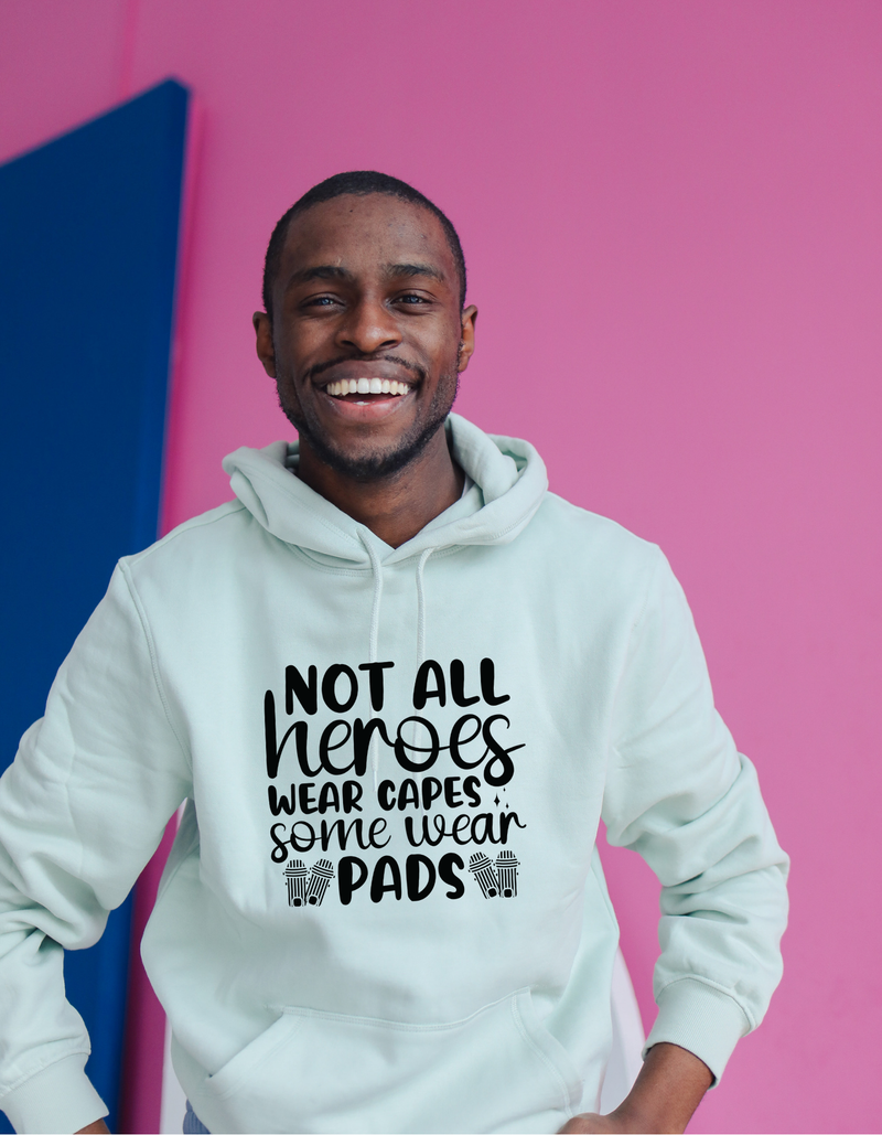 A man wearing a white hoodie with Not All Heroes Wear Capes, Some Wear Pads on the front. A Funny Cricket Hoodie, Premium Fabric, Multiple Adult Sizes