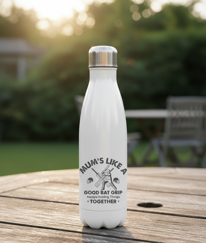 White water bottle with a printed design on a wooden table outdoors. This is a Cows Corner water bottle with a funny cricket slogan 'Mums Like A Good Bat Grip, Always Holding Things Together'. Cows Corner gifts are perfect for sport-mad fans, these gifts work brilliantly for birthdays, new baby celebrations, Father’s Day, Mother’s Day, Christmas, anniversaries, thank you gifts, end-of-season team awards, graduations, retirements, and just-because moments when you want to raise a smile. 
