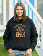 A lady wearing a black hoodie with You Bring the Sledging, I'll Bring the Sixes on the front. A Funny Cricket Hoodie, Premium Fabric, Multiple Adult Sizes