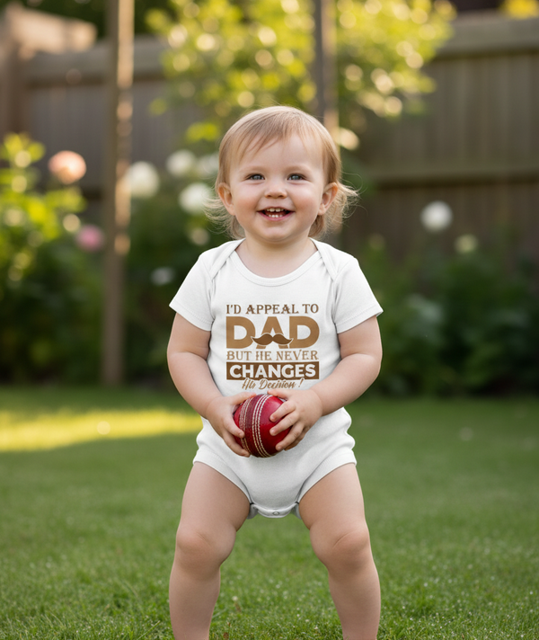 Child wearing a onesie with text holding a ball outdoors. The baby is wearing a Cows Corner baby grow with a funny cricket slogan 'I'd Appeal to Dad, But He Never Changes His Decision'. Cows Corner gifts are perfect for sport-mad fans, these gifts work brilliantly for birthdays, new baby celebrations, Father’s Day, Mother’s Day, Christmas, anniversaries, thank you gifts, end-of-season team awards, graduations, retirements, and just-because moments when you want to raise a smile. 
