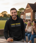 Man wearing a black hoodie with humorous text, sitting outdoors with friends. The man is wearing a Cows Corner hoodie with a funny cricket slogan 'I Don't Block, Only Bash'. Cows Corner gifts are perfect for sport-mad fans, these gifts work brilliantly for birthdays, new baby celebrations, Father’s Day, Mother’s Day, Christmas, anniversaries, thank you gifts, end-of-season team awards, graduations, retirements, and just-because moments when you want to raise a smile. 
