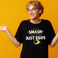 A man wearing a black t-shirt that has a funny tennis slogan on the front that reads 'I Don't Smash Rackets Just Egos'