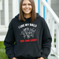 A lady wearing a black hoodie with I Like My Balls Red And Hard on the front. A Funny Cricket Hoodie, Premium Fabric, Multiple Adult Sizes