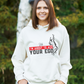 A lady wearing a white hoodie with the funny tennis slogan on the front that reads 'Shh....i'm About To Ace Your Ego'
