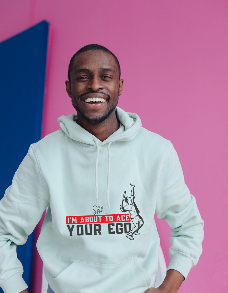 A man wearing a white hoodie with the funny tennis slogan on the front that reads 'Shh....i'm About To Ace Your Ego'