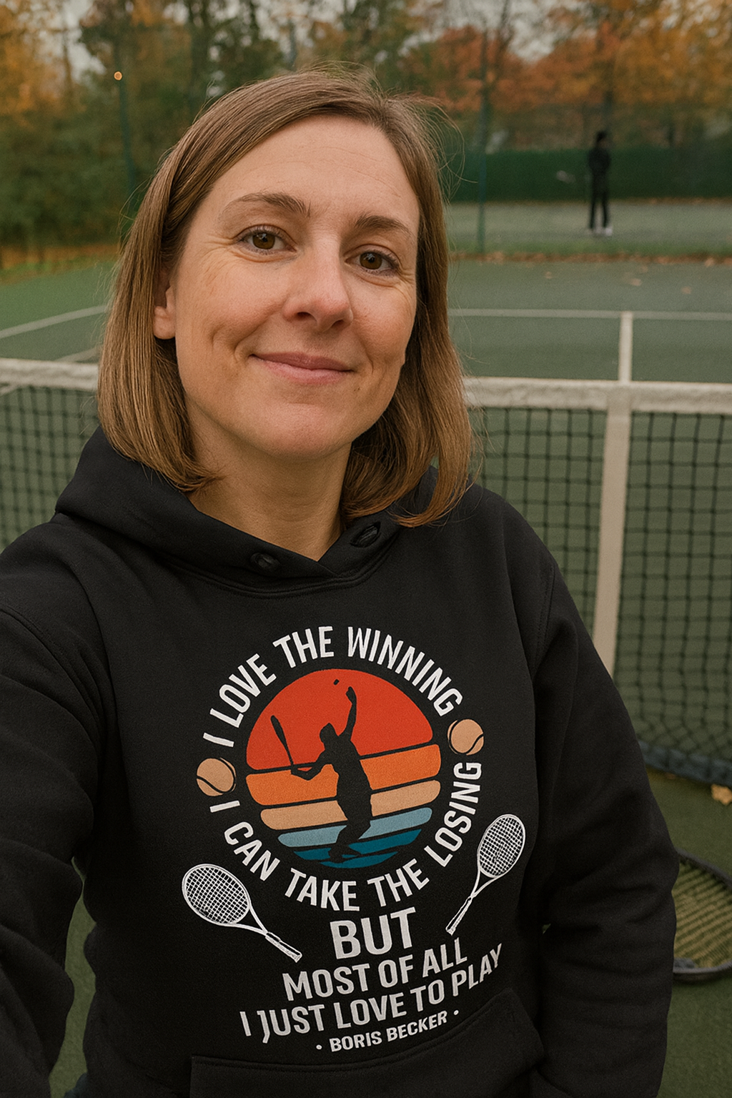 Person wearing a black hoodie with a graphic design on a tennis court.  Hoodie is from Cows Corner and has the slogan on the front saying 'I Love the Winning, I Can’t Take the Losing, but Most of All I Just Love To Play' 