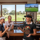 Three women in a golf club lounge with drinks, watching a golf game on TV. The lady is wearing a Cows Corner t-shirt with the funny golf slogan on the front that reads 'Your Swing Is Like a Horror Movie, Ugly and Full of Screams'. Cows Corner gifts are perfect for sport-mad fans, these gifts work brilliantly for birthdays, new baby celebrations, Father’s Day, Mother’s Day, Christmas, anniversaries, thank you gifts, end-of-season team awards, graduations, retirements, and just-because moments 