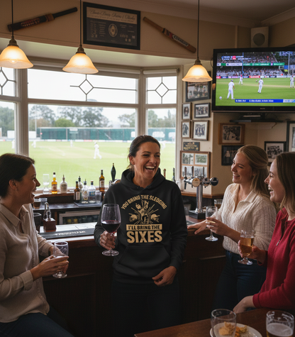 A lady wearing a Cows Corner hoodie with the funny cricket slogan that reads 'You Bring The Sledging, I'll Bring The Sixes'.  Cows Corner gifts are perfect for sport-mad fans, these gifts work brilliantly for birthdays, new baby celebrations, Father’s Day, Mother’s Day, Christmas, anniversaries, thank you gifts, end-of-season team awards, graduations, retirements, and just-because moments when you want to raise a smile. 
