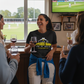 A lady standing in her local cricket club wearing a Cows Corner funny t-shirt with the funny slogan on the front that reads 'I like my pitches hard and my balls shiny!'