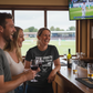 People enjoying drinks and watching a game on TV in a pub with the lady wearing a Cows Corner t-shirt with the funny slogan on the front saying 'Nice length shame about the width'. Cows Corner gifts are perfect for sport-mad fans who love a bit of humour and personality in their presents. They’re ideal for friends, partners, parents, coaches, teammates, and proud mums and dads who live and breathe sport, whether they play, watch from the sidelines, or shout at the telly every weekend. These gifts work