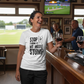 Woman in a bar wearing a t-shirt with a cricket-themed message, holding a glass of wine.  The lady is wearing a Cows Corner t-shirt with the funny cricket saying on the front that reads 'Stop Staring At My Middle Stump'