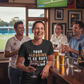 People in a pub watching a sports match on TV, with one person holding a glass.  The lady is wearing a Cows Corner t-shirt with the funny cricket slogan on the front that says 'Your Sledging Is As Soft As Your Bowling'