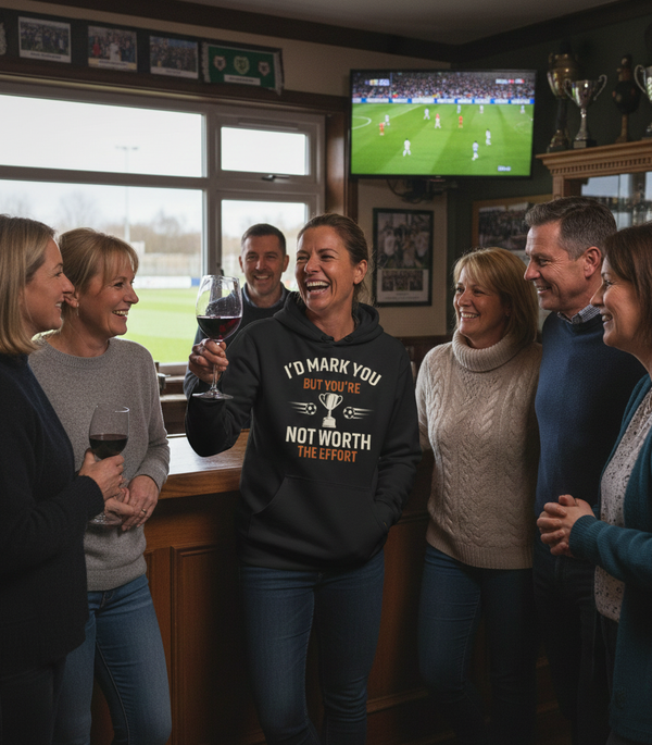 Group of people in a pub watching a sports match on television. The lady is wearing a Cows Corner hoodie with the funny football slogan 'I’d Mark You but You’re Not Worth the Effort'. Cows Corner gifts are perfect for sport-mad fans, these gifts work brilliantly for birthdays, new baby celebrations, Father’s Day, Mother’s Day, Christmas, anniversaries, thank you gifts, end-of-season team awards, graduations, retirements, and just-because moments when you want to raise a smile. 
