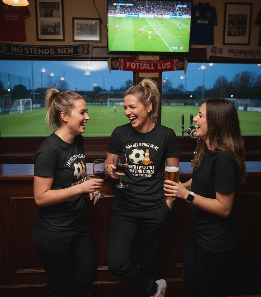 Three women in a bar watching sports on TV with drinks.  The lady is wearing a Cows Corner t-shirt with the football slogan on the front that reads 'For Believing in Me When I Was Still Chasing Cones – Thank You, Coach'. Cows Corner gifts are perfect for sport-mad fans, these gifts work brilliantly for birthdays, new baby celebrations, Father’s Day, Mother’s Day, Christmas, anniversaries, thank you gifts, end-of-season team awards, graduations, retirements, and just-because moments 