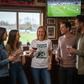 Group of people watching a football match on TV in a pub.  The lady is wearing a Cows Corner T-shirt with the funny football slogan on the front that reads 'Thanks Coach From the First Touch to Final Whistle, You’ve Been the Heat of It All'. Cows Corner gifts are perfect for sport-mad fans, these gifts work brilliantly for birthdays, new baby celebrations, Father’s Day, Mother’s Day, Christmas, anniversaries, thank you gifts, end-of-season team awards, graduations, retirements, and just-because moments