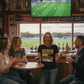 People watching a sports game on TV in a pub with a woman in a Cows Corner T-shirt with the funny football slogan on the front that reads 'Your First Tough Choice Is A Crime Against Football'.  Cows Corner gifts are perfect for sport-mad fans, these gifts work brilliantly for birthdays, new baby celebrations, Father’s Day, Mother’s Day, Christmas, anniversaries, thank you gifts, end-of-season team awards, graduations, retirements, and just-because moments when you want to raise a smile. 