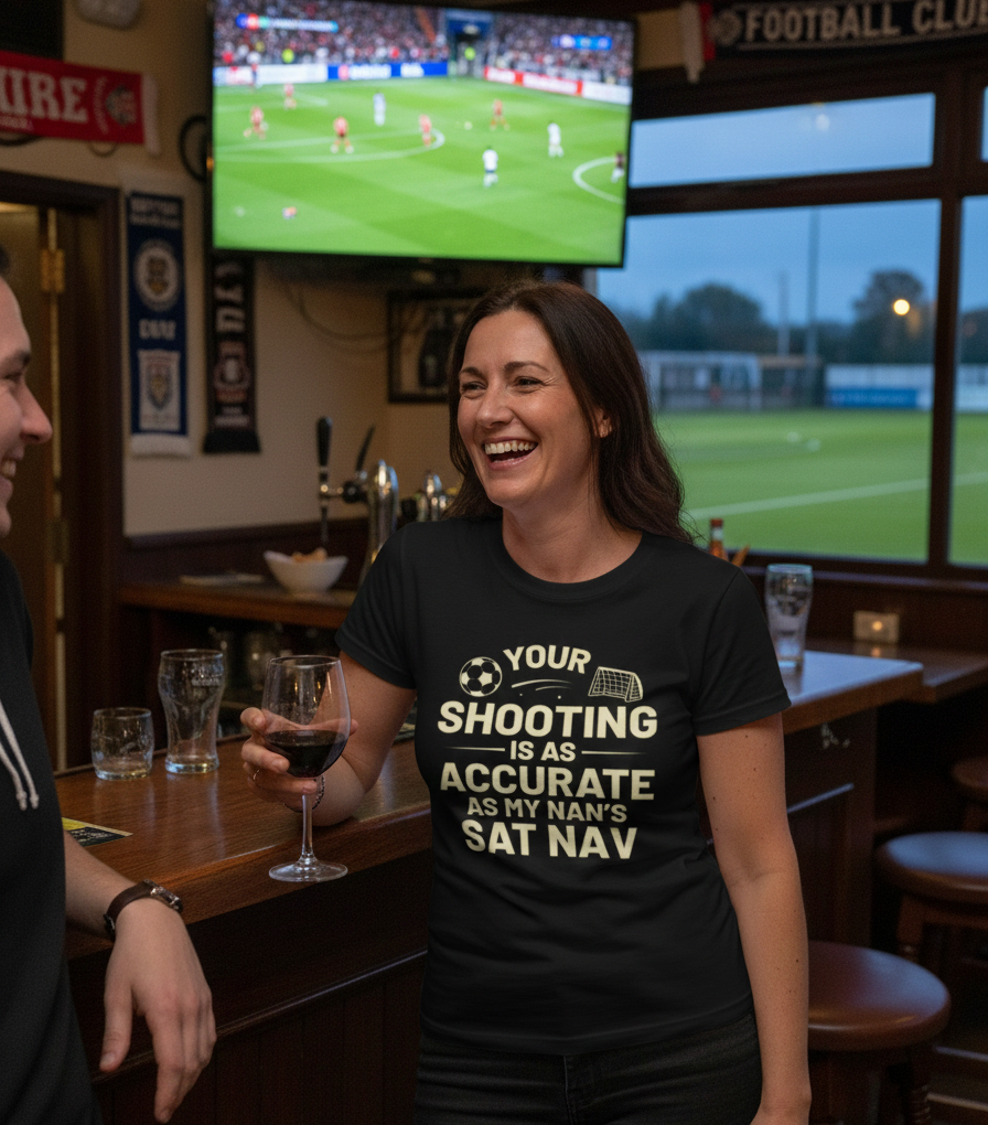 Woman in a bar wearing a humorous t-shirt, watching sports on TV.  The lady is wearing a Cows Corner t-shirt with the funny football slogan on the front that reads 'Your First Touch Is a Crime Against Football'. Cows Corner gifts are perfect for sport-mad fans, these gifts work brilliantly for birthdays, new baby celebrations, Father’s Day, Mother’s Day, Christmas, anniversaries, thank you gifts, end-of-season team awards, graduations, retirements, and just-because moments when you want to raise a smile.