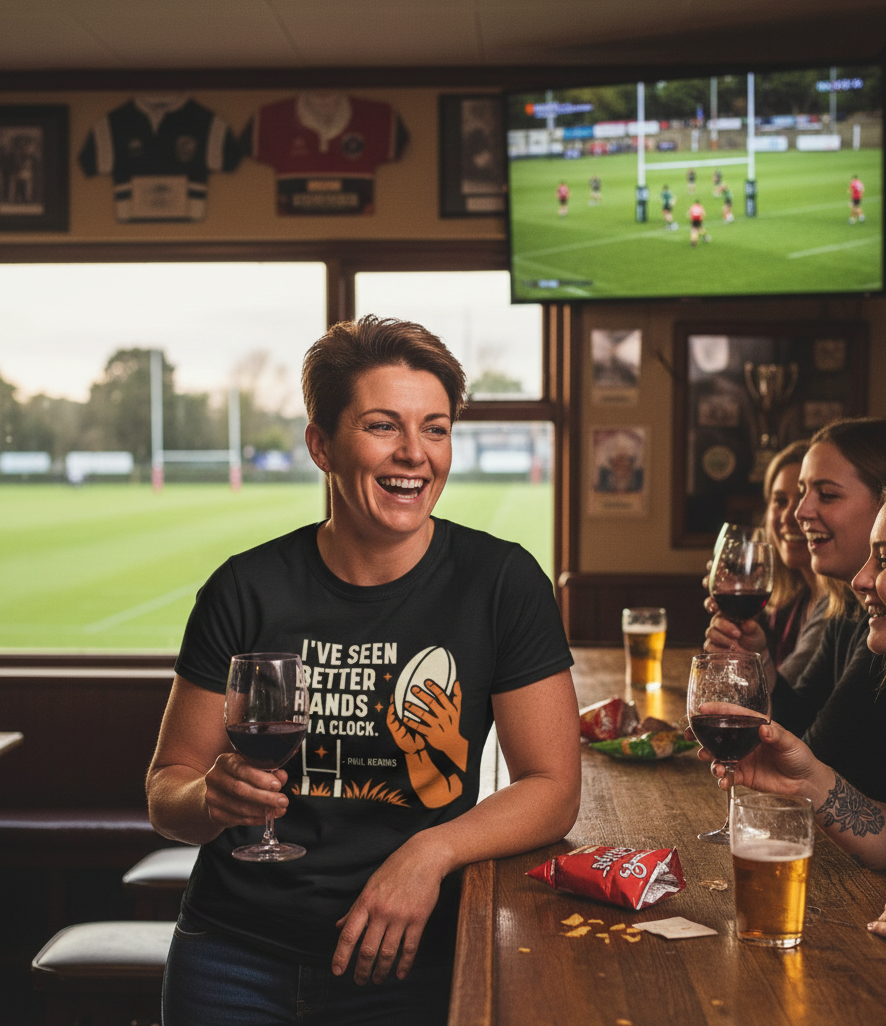 People enjoying drinks and watching a sports match in a pub. The lady is wearing a Cows Corner t-shirt with the funny rugby slogan 'I’ve Seen Better Hands on a Clock – Phil Kearns'. Cows Corner gifts are perfect for sport-mad fans, these gifts work brilliantly for birthdays, new baby celebrations, Father’s Day, Mother’s Day, Christmas, anniversaries, thank you gifts, end-of-season team awards, graduations, retirements, and just-because moments when you want to raise a smile. 
