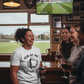 People in a pub watching a sports match on television, one person wearing a t-shirt with a running-themed design. The lady is wearing a Cows Corner t-shirt with the funny rugby slogan on the front that reads 'Run at Me I Dare You'. Cows Corner gifts are perfect for sport-mad fans, these gifts work brilliantly for birthdays, new baby celebrations, Father’s Day, Mother’s Day, Christmas, anniversaries, thank you gifts, end-of-season team awards, graduations, retirements, and just-because moments 
