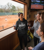 Three women in a tennis club, one wearing a hoodie.  The lady is wearing a Cows Corner hoodie with the funny tennis slogan 'Your Serve Is As Weak As Your Excuses'.  Cows Corner gifts are perfect for sport-mad fans, these gifts work brilliantly for birthdays, new baby celebrations, Father’s Day, Mother’s Day, Christmas, anniversaries, thank you gifts, end-of-season team awards, graduations, retirements, and just-because moments when you want to raise a smile. 
