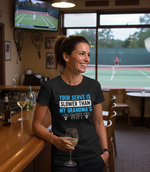 Woman in a bar wearing a t-shirt with humorous text, with tennis court visible in the background.  The lady is wearing a Cows Corner T-shirt with the funny tennis slogan on the front that reads 'Your Serve Is Slower Than My Grandma's Wifi'.  Cows Corner gifts are perfect for sport-mad fans, these gifts work brilliantly for birthdays, new baby celebrations, Father’s Day, Mother’s Day, Christmas, anniversaries, thank you gifts, end-of-season team awards, graduations, retirements, and just-because moments.