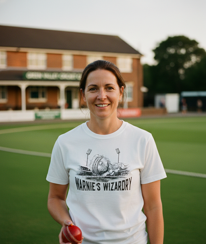 Woman wearing a 'Warnie's Wizardry' t-shirt on a sports field with a building in the background. The lady is wearing a Cows Corner t-shirt with the funny cricket slogan 'Warnie’s Wizardry'. Cows Corner gifts are perfect for sport-mad fans, these gifts work brilliantly for birthdays, new baby celebrations, Father’s Day, Mother’s Day, Christmas, anniversaries, thank you gifts, end-of-season team awards, graduations, retirements, and just-because moments when you want to raise a smile. 
