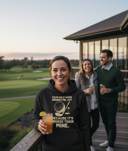 Woman in a hoodie with a golf-themed message, holding a drink, with a golf course and building in the background. The lady is wearing a Cows Corner hoodie with a funny golf slogan 'Your Golf Game Bring Me Joy, Because It’s Worse Than Mine'. Cows Corner gifts are perfect for sport-mad fans, these gifts work brilliantly for birthdays, new baby celebrations, Father’s Day, Mother’s Day, Christmas, anniversaries, thank you gifts, end-of-season team awards, graduations, retirements, and just-because moments 