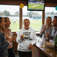 Group of people enjoying drinks and watching a sports game in a pub. The lady is wearing a Cows Corner hoodie with the funny cricket birthday slogan 'Forget the 'Googly', at your age, it’s just a 'Saggy''. Cows Corner gifts are perfect for sport-mad fans, these gifts work brilliantly for birthdays, new baby celebrations, Father’s Day, Mother’s Day, Christmas, anniversaries, thank you gifts, end-of-season team awards, graduations, retirements, and just-because moments when you want to raise a smile. 
