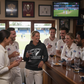 Group of people in sports attire gathered around a bar, watching a game on television. The lady is wearing a Cows Corner hoodie with the funny cricket birthday slogan 'Happy Birthday! May Your Balls Be Shiny and Your Wood Be Hard.'  Cows Corner gifts are perfect for sport-mad fans, these gifts work brilliantly for birthdays, new baby celebrations, Father’s Day, Mother’s Day, Christmas, anniversaries, thank you gifts, end-of-season team awards, graduations, retirements, and just-because moments 