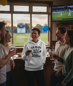 Group of people celebrating a birthday in a sports bar with a TV showing a cricket match. The lady is wearing a Cows Corner hoodie with the funny cricket birthday slogan 'Old, Bold & Still Looking for a Decent Length. Happy Birthday'.  Cows Corner gifts are perfect for sport-mad fans, these gifts work brilliantly for birthdays, new baby celebrations, Father’s Day, Mother’s Day, Christmas, anniversaries, thank you gifts, end-of-season team awards, graduations, retirements, and just-because moments when you w