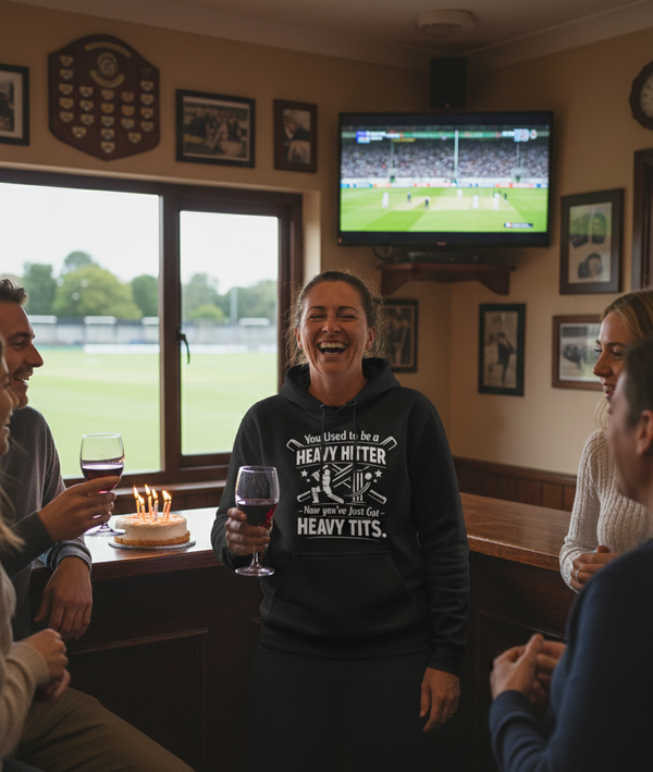 People in a pub watching a sports match on TV, one person wearing a humorous hoodie. The lady is wearing a Cows Corner hoodie with the funny cricket birthday slogan 'You Used to be a Heavy Hitter. Now you’ve Just Got Heavy Tits'. Cows Corner gifts are perfect for sport-mad fans, these gifts work brilliantly for birthdays, new baby celebrations, Father’s Day, Mother’s Day, Christmas, anniversaries, thank you gifts, end-of-season team awards, graduations, retirements, and just-because moments 