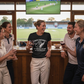 Group of people in cricket uniforms celebrating a birthday with drinks in a bar.  The lady is wearing a Cows Corner t-shirt with the funny cricket birthday slogan 'Happy Birthday! May Your Balls Be Shiny and Your Wood Be Hard.' Cows Corner gifts are perfect for sport-mad fans, these gifts work brilliantly for birthdays, new baby celebrations, Father’s Day, Mother’s Day, Christmas, anniversaries, thank you gifts, end-of-season team awards, graduations, retirements, and just-because moments 