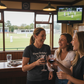 Three women in a pub enjoying drinks and watching a game on TV. The lady is wearing a Cows Corner t-shirt with the funny birthday cricket slogan 'Happy Birthday! May your wood be firm and your balls stay red'. Cows Corner gifts are perfect for sport-mad fans, these gifts work brilliantly for birthdays, new baby celebrations, Father’s Day, Mother’s Day, Christmas, anniversaries, thank you gifts, end-of-season team awards, graduations, retirements, and just-because moments when you want to raise a smile. 
