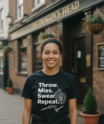 Person wearing a black t-shirt with text and graphics in front of a pub.  This is a Cows Corner t-shirt with the funny darts slogan 'Throw. Miss. Swear. Repeat'. Cows Corner gifts are perfect for sport-mad fans, these gifts work brilliantly for birthdays, new baby celebrations, Father’s Day, Mother’s Day, Christmas, anniversaries, thank you gifts, end-of-season team awards, graduations, retirements, and just-because moments when you want to raise a smile. 
