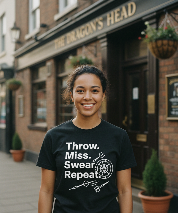 Person wearing a black t-shirt with text and graphics in front of a pub.  This is a Cows Corner t-shirt with the funny darts slogan 'Throw. Miss. Swear. Repeat'. Cows Corner gifts are perfect for sport-mad fans, these gifts work brilliantly for birthdays, new baby celebrations, Father’s Day, Mother’s Day, Christmas, anniversaries, thank you gifts, end-of-season team awards, graduations, retirements, and just-because moments when you want to raise a smile. 
