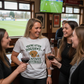 Group of women in a pub watching a sports game on television, one wearing a humorous t-shirt. The lady is wearing a Cows Corner t-shirt with the funny fantasy football slogan on the front that reads 'You're Utter Dogsh*t at Fantasy Football'. Cows Corner gifts are perfect for sport-mad fans, these gifts work brilliantly for birthdays, new baby celebrations, Father’s Day, Mother’s Day, Christmas, anniversaries, thank you gifts, end-of-season team awards, graduations, retirements, and just-because moments