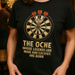 Person wearing a black t-shirt with a dartboard graphic and text in a casual setting with a Cows Corner slogan The oche where legends are made and excuses are born.