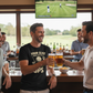 Two men clinking beer glasses in a bar with a TV showing a golf game in the background.  The man is wearing a Cows Corner t-shirt with a funny golf slogan on the front that reads 'Your Slice Should Come With a GPS'. Cows Corner gifts are perfect for sport-mad fans, these gifts work brilliantly for birthdays, new baby celebrations, Father’s Day, Mother’s Day, Christmas, anniversaries, thank you gifts, end-of-season team awards, graduations, retirements, and just-because moments when you want to raise a smile