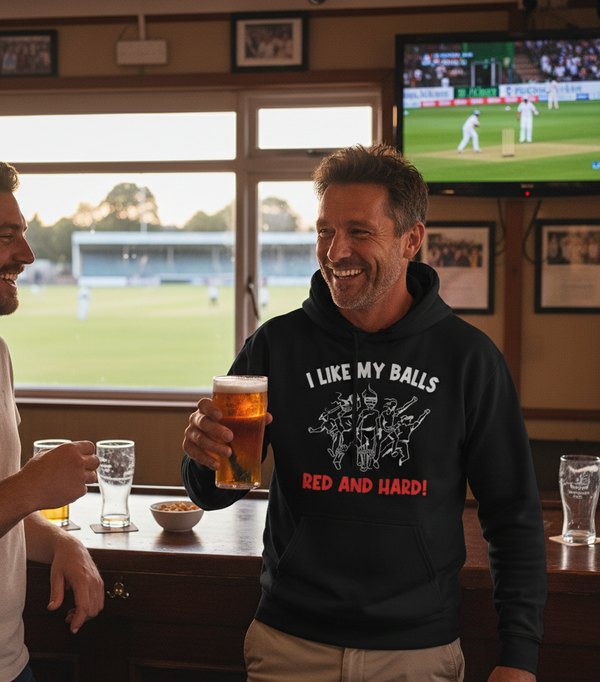 Two men in a pub, one holding a beer, with a sports game on a screen in the background. The man is wearing a Cows Corner hoodie with the funny cricket slogan that reads 'I Like My Balls Red And Hard'.  Cows Corner gifts are perfect for sport-mad fans, these gifts work brilliantly for birthdays, new baby celebrations, Father’s Day, Mother’s Day, Christmas, anniversaries, thank you gifts, end-of-season team awards, graduations, retirements, and just-because moments when you want to raise a smile. 
