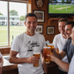 Group of men enjoying beers together in a pub with a cricket match on TV.  The man is wearing a Cows Corner T-shirt with the funny cricket slogan on the front that reads 'I Bat in the Middle of a Hat-trick'.  Cows Corner gifts are perfect for sport-mad fans, these gifts work brilliantly for birthdays, new baby celebrations, Father’s Day, Mother’s Day, Christmas, anniversaries, thank you gifts, end-of-season team awards, graduations, retirements, and just-because moments when you want to raise a smile.
