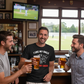Three men in a pub enjoying drinks and watching a cricket match on TV.  The man is wearing a Cows Corner t-shirt with the funny cricket saying on the front which says 'I Like My Balls Red And Hard