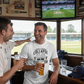 Two men in a sports bar watching a cricket match on TV, one wearing a Cows Corner T-shirt with the funny cricket slogan on the front that reads 'Middle-Order Collapse Survivor'. Cows Corner gifts are perfect for sport-mad fans, these gifts work brilliantly for birthdays, new baby celebrations, Father’s Day, Mother’s Day, Christmas, anniversaries, thank you gifts, end-of-season team awards, graduations, retirements, and just-because moments when you want to raise a smile. 