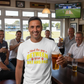Man in a pub wearing a t-shirt with a humorous cricket-related message, holding a beer.  The man is wearing a Cows Corner T-shirt with the funny cricket slogan on the front saying 'Mind The Gap Between Your Bat And Pads'.