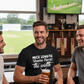 Three men in a pub watching cricket on TV, one holding a beer wearing a Cows Corner T-shirt with the funny slogan on the front saying 'Nice length shame about the width'. Cows Corner gifts are perfect for sport-mad fans who love a bit of humour and personality in their presents. They’re ideal for friends, partners, parents, coaches, teammates, and proud mums and dads who live and breathe sport, whether they play, watch from the sidelines, or shout at the telly every weekend. These gifts work brilliantly