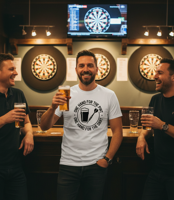 Three men in a bar with drinks, smiling and posing for a photo in front of dartboards. The man is wearing a Cows Corner t-shirt with the funny darts slogan 'One Hand For The Pint, One Hand For The Darts'. Cows Corner gifts are perfect for sport-mad fans, these gifts work brilliantly for birthdays, new baby celebrations, Father’s Day, Mother’s Day, Christmas, anniversaries, thank you gifts, end-of-season team awards, graduations, retirements, and just-because moments when you want to raise a smile. 

