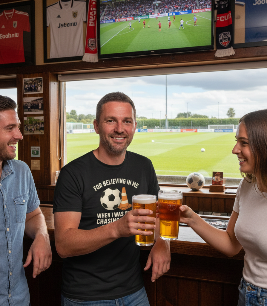 Three people in a sports bar watching a soccer match on TV.  The man is wearing a Cows Corner t-shirt with the football slogan on the front that reads For Believing in Me When I Was Still Chasing Cones – Thank You, Coach'. Cows Corner gifts are perfect for sport-mad fans, these gifts work brilliantly for birthdays, new baby celebrations, Father’s Day, Mother’s Day, Christmas, anniversaries, thank you gifts, end-of-season team awards, graduations, retirements, and just-because moments 