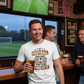 Man in a bar wearing a t-shirt with a football-themed design, holding a beer. The man is wearing a Cows Corner T-shirt with a funny football slogan on the front which reads 'If Football Was Easy You’d Be Good at It'.  Cows Corner gifts are perfect for sport-mad fans, these gifts work brilliantly for birthdays, new baby celebrations, Father’s Day, Mother’s Day, Christmas, anniversaries, thank you gifts, end-of-season team awards, graduations, retirements, and just-because moments 
